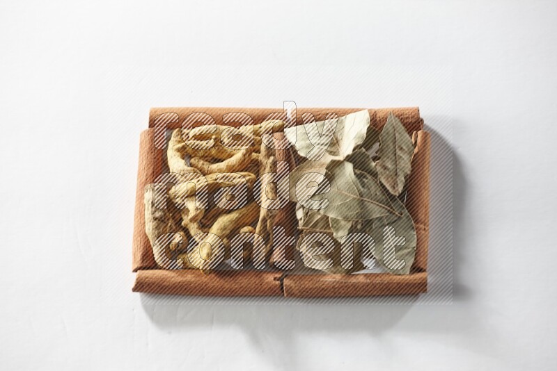 2 squares of cinnamon sticks full of turmeric fingers and bay laurel leaves on white flooring