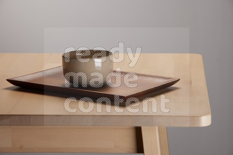multicolored bowl placed on a rectangular wooden tray on the edge of wooden table