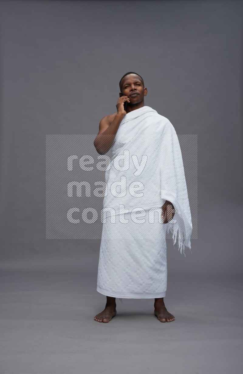 A man wearing Ehram Standing texting on phone on gray background