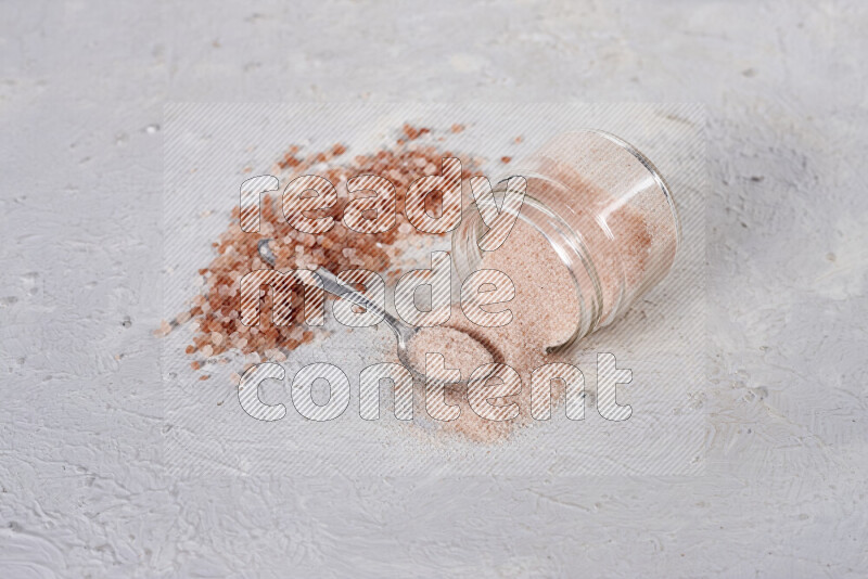 A glass jar full of fine himalayan salt with some himalayan crystals beside it on a white background