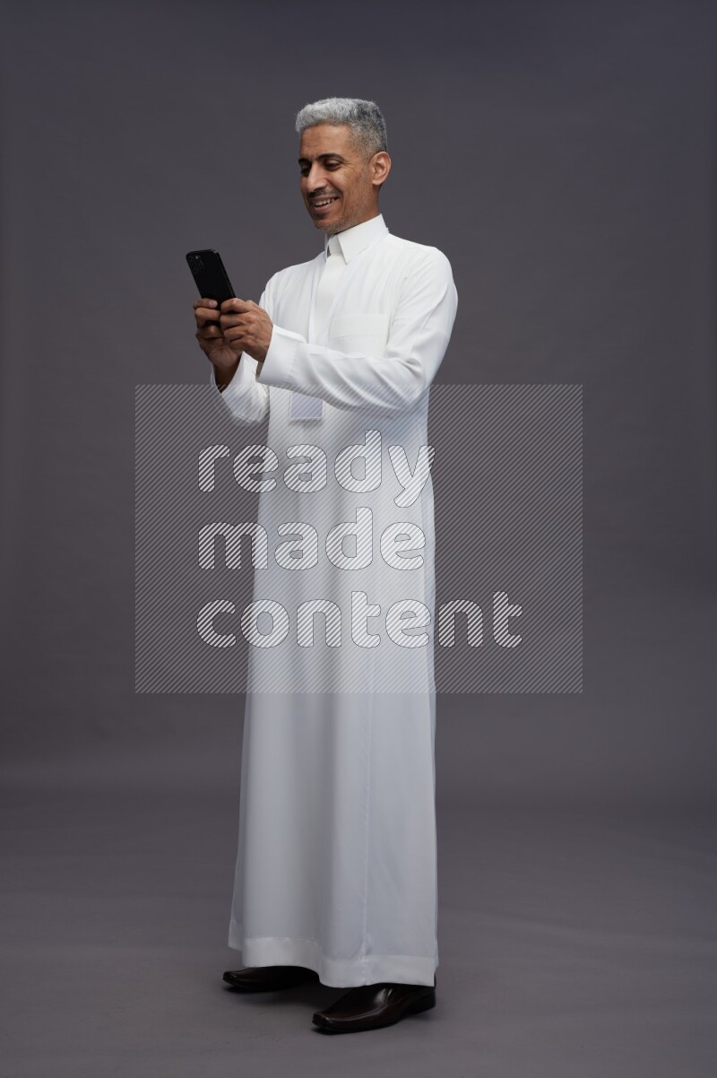 Saudi man wearing thob with neck strap employee badge standing texting on phone on gray background