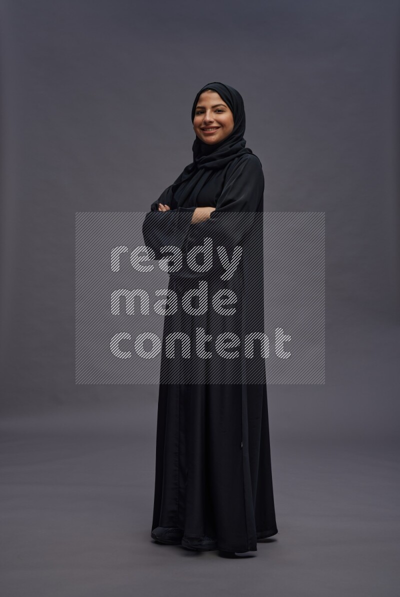 Saudi woman wearing Abaya standing with crossed arms on gray background