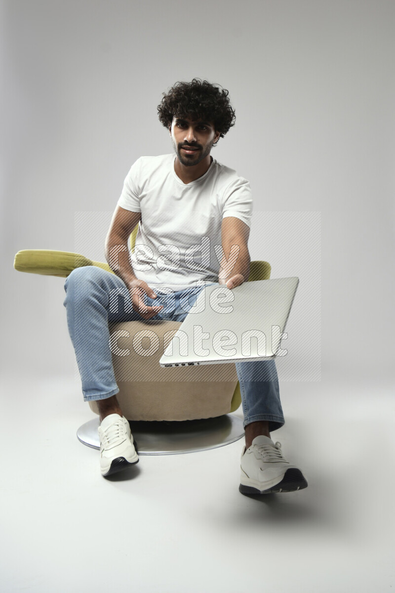A man wearing casual sitting on a chair holding a laptop on white background