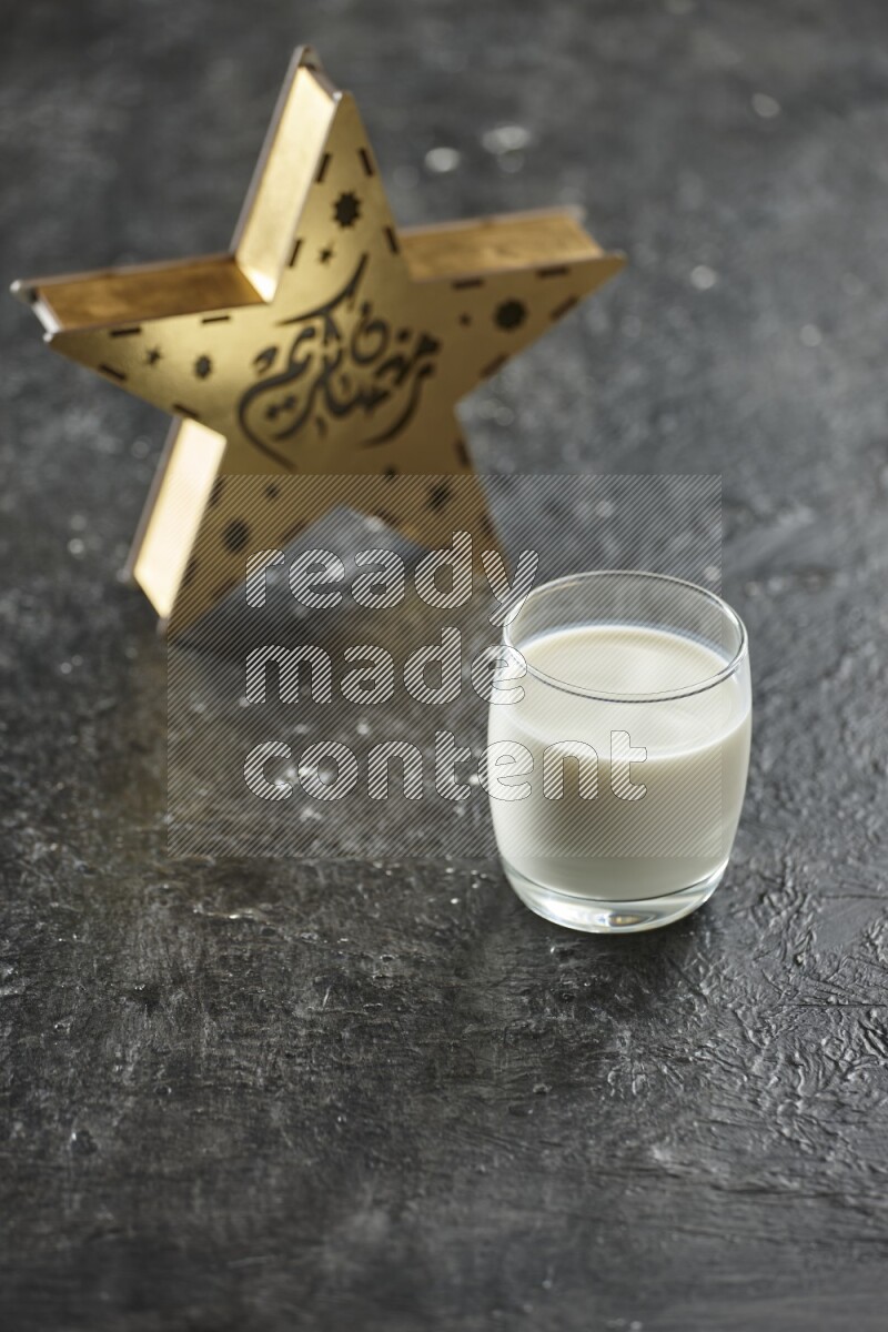A wooden golden star lantern with different drinks, dates, nuts, prayer beads and quran on textured black background