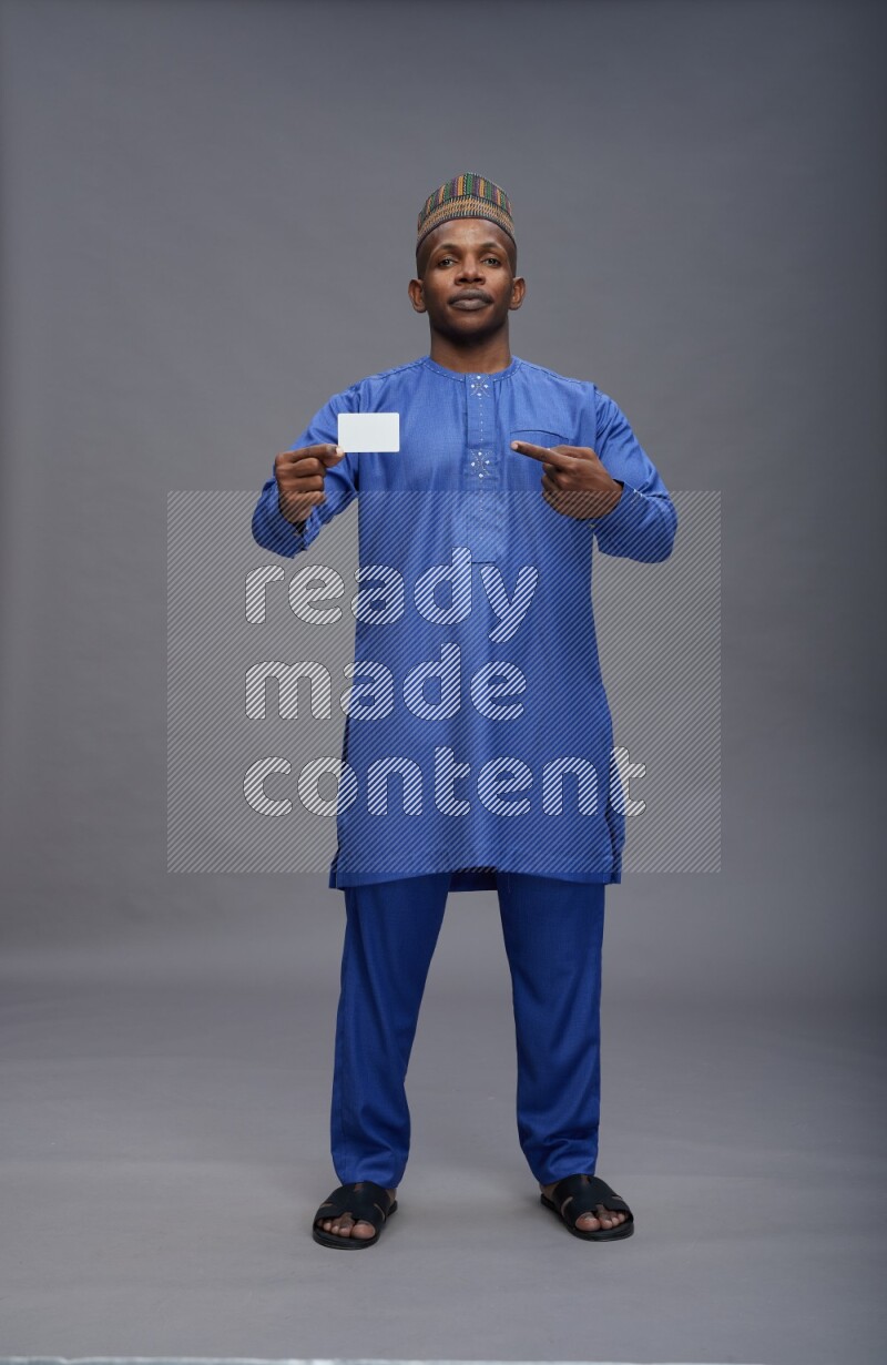 Man wearing Nigerian outfit standing holding ATM card on gray background
