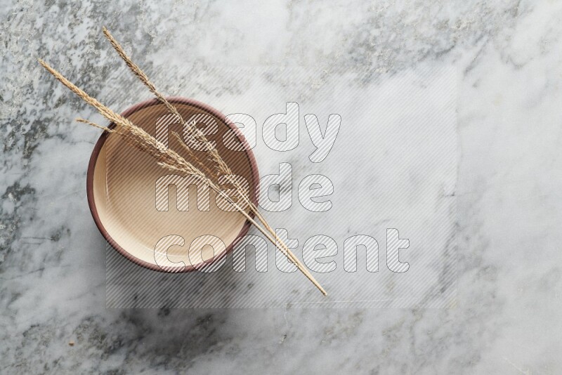 Wheat stalks on beige pottery oven bowl on grey marble background