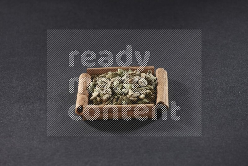 أربعة من أعواد القرفة مكونة شكل مربع بداخلها حبوب الهيل علي خلفية سوداء