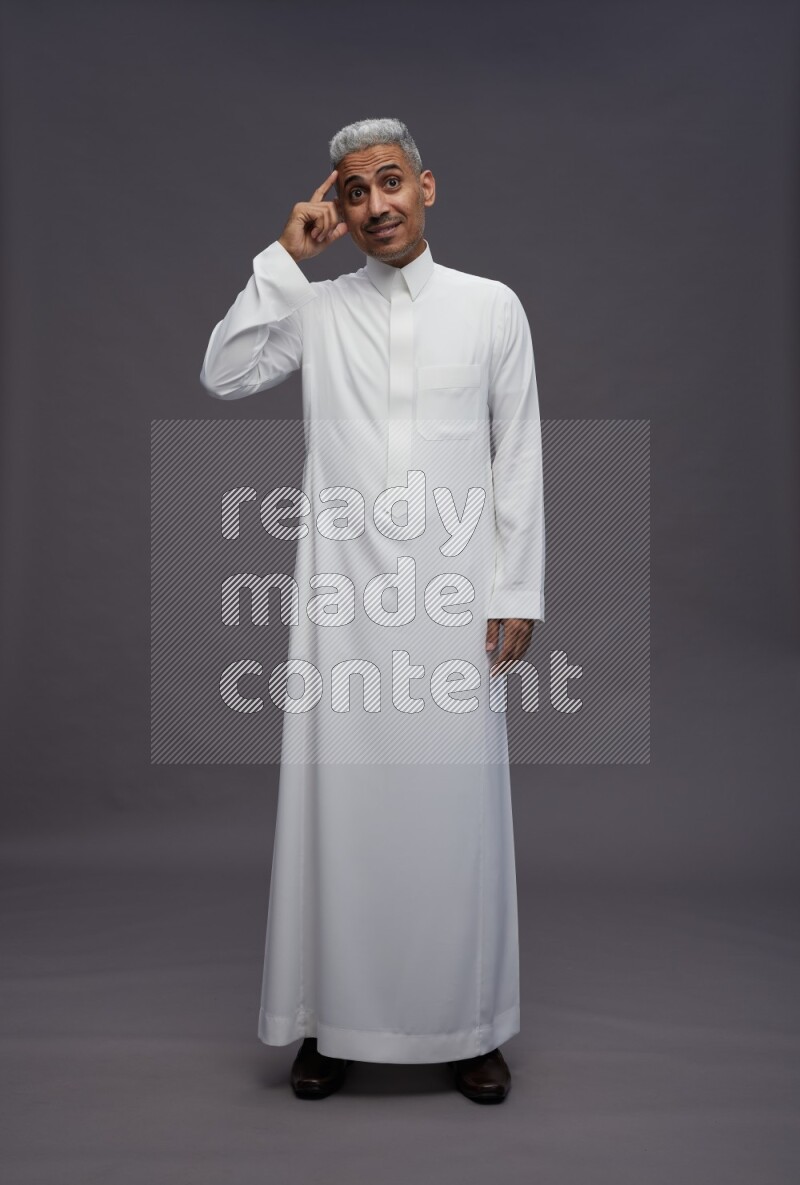 Saudi man wearing thob standing interacting with the camera on gray background