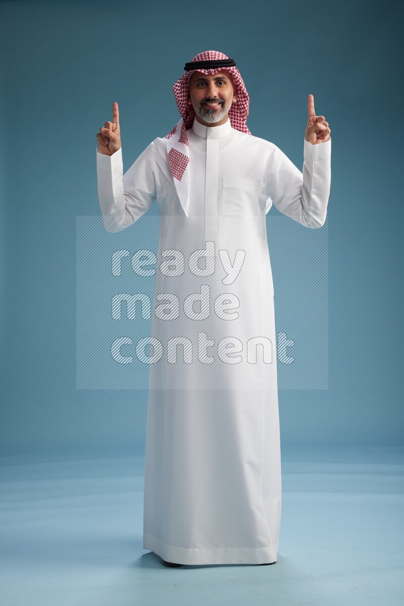 Saudi man wearing thob and shomagh posing to the camera on blue background