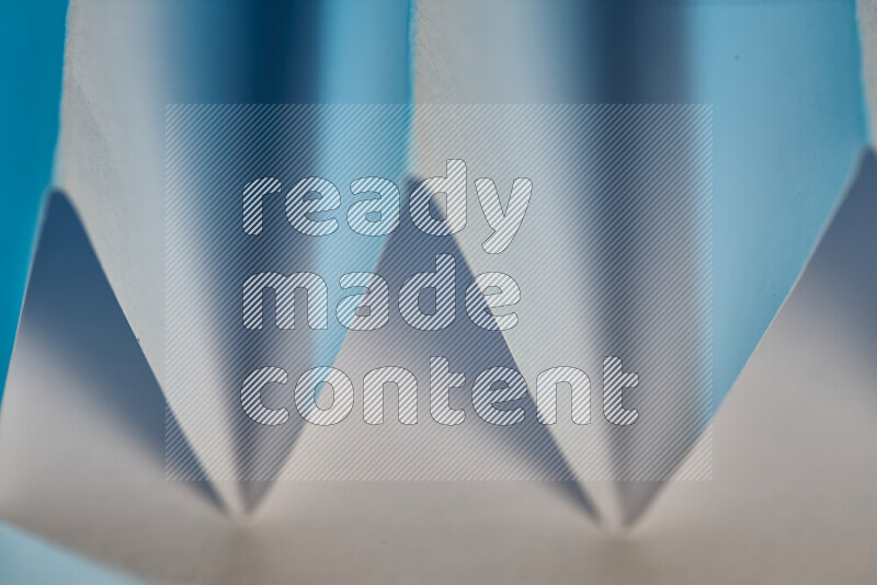 A close-up abstract image showing sharp geometric paper folds in white and blue gradients