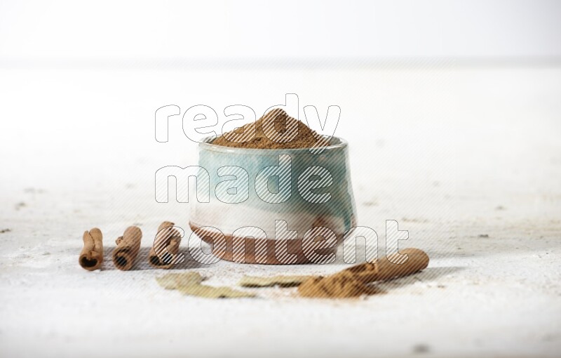 Cinnamon powder in a ceramic bowl with cinnamon sticks and laurel leaves on white background