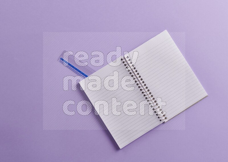 A blank open notebook with school supplies on purple background