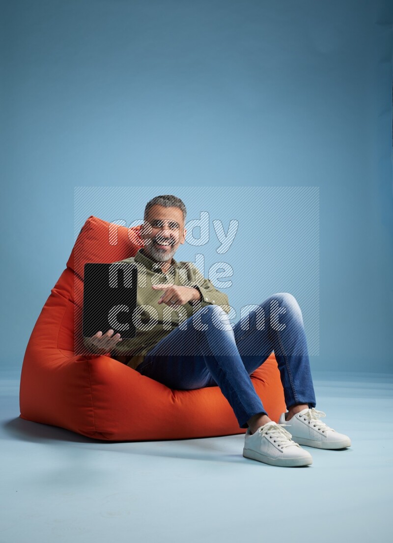 A man sitting on an orange beanbag and working on tablet
