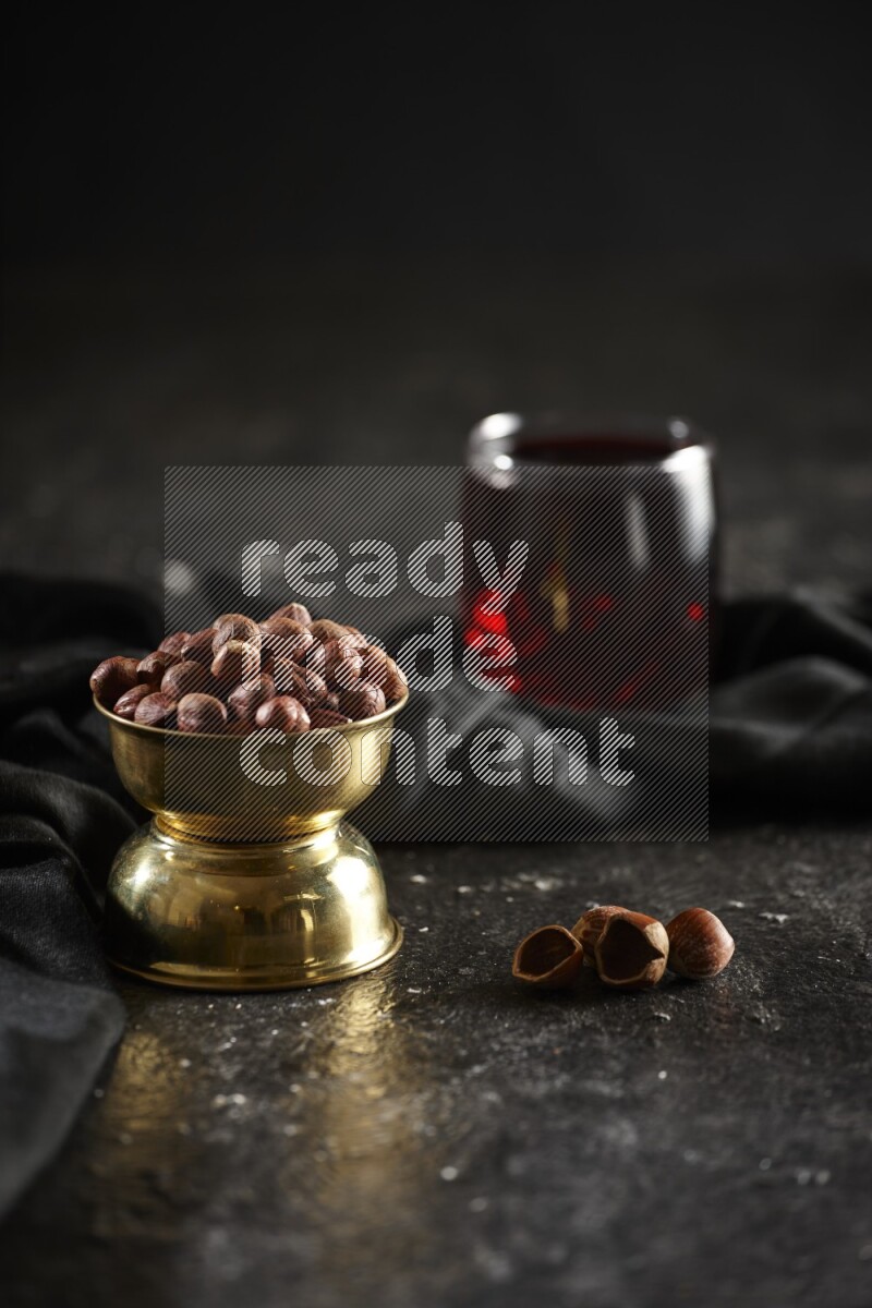Nuts in a metal bowl with hibiscus and a napkin in a dark setup