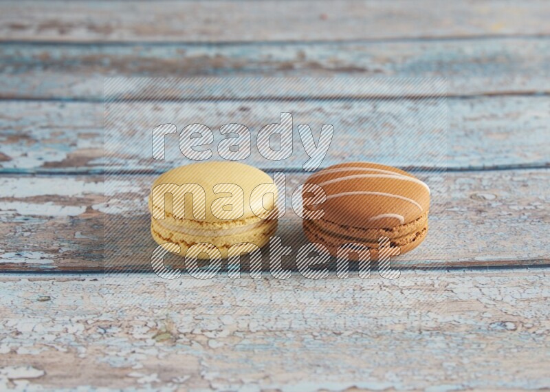 45º Shot of of two assorted Brown Irish Cream, and Yellow Vanilla macarons on light blue background
