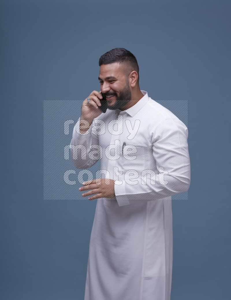 A Saudi man calling on blue background wearing Saudi Thob