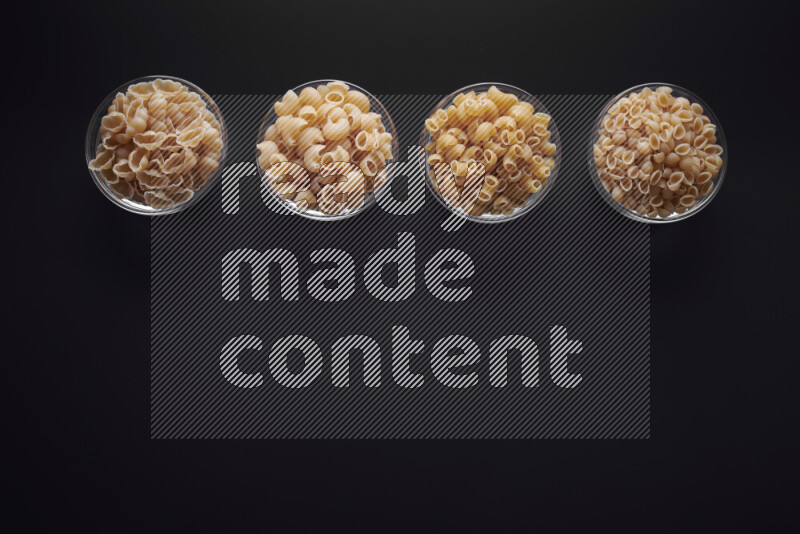 Different pasta types in glass bowls on black background