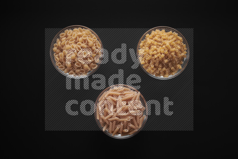 Different pasta types in glass bowls on black background