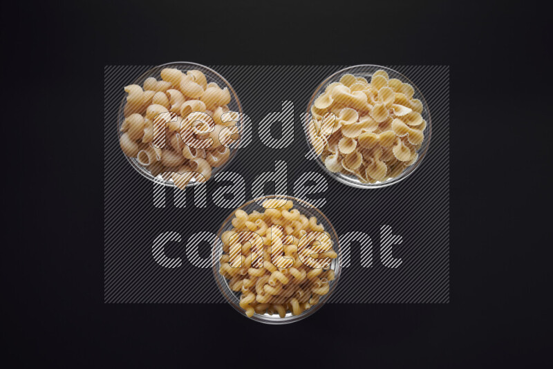 Different pasta types in glass bowls on black background