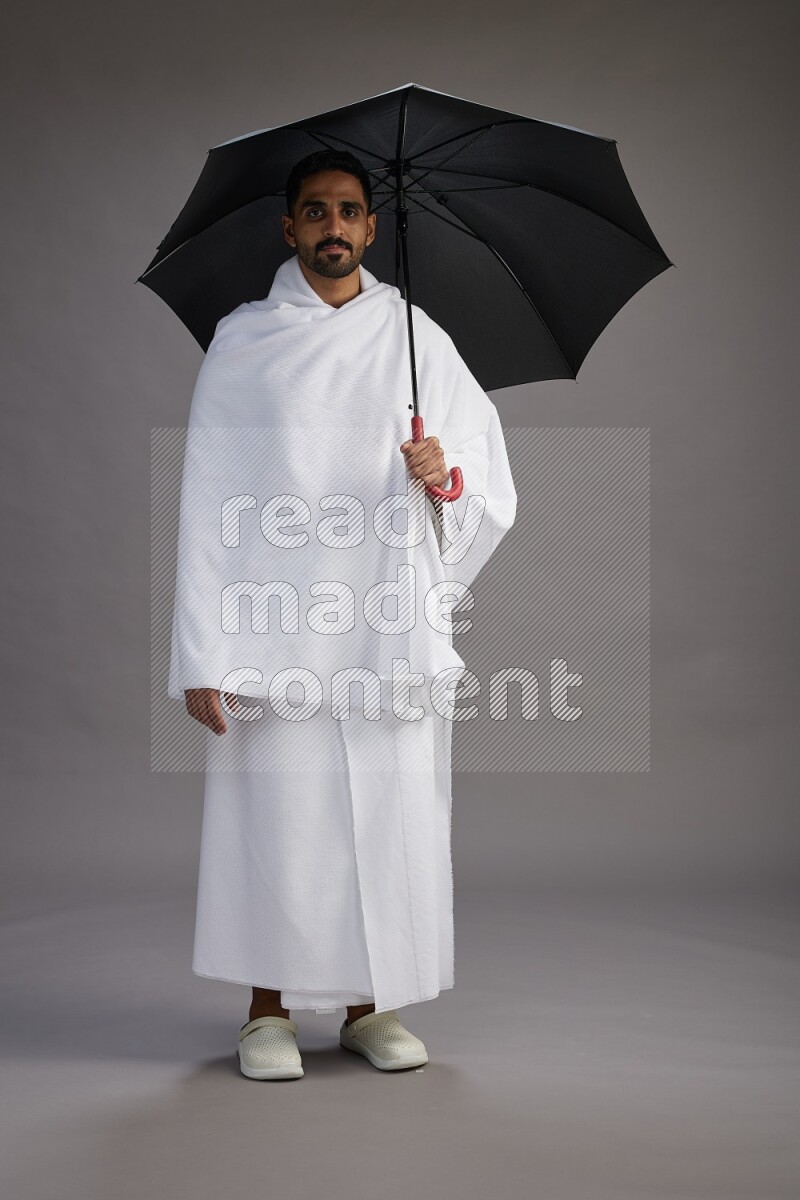 A man wearing Ehram Standing holding umbrella on gray background