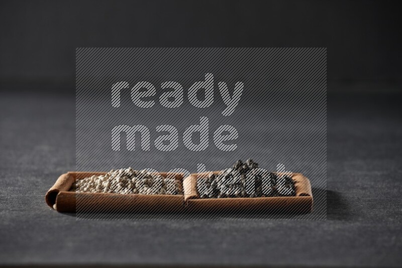 2 squares of cinnamon sticks full of white peppers and black peppers on black flooring