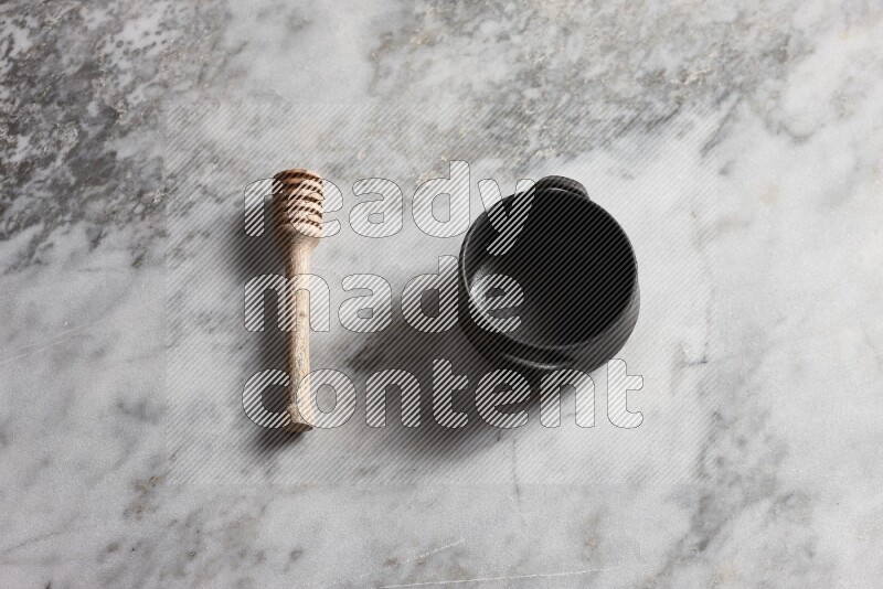 Black pottery bowl with wooden honey dipper on the side on grey marble background