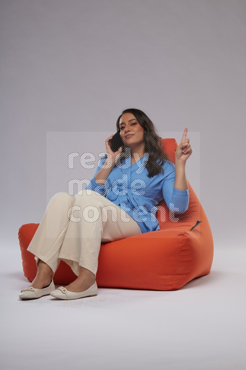 A woman sitting on an orange beanbag and talking on the phone