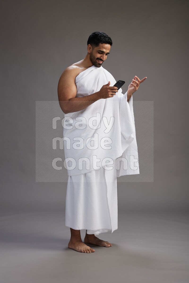 A man wearing Ehram Standing texting on phone on gray background