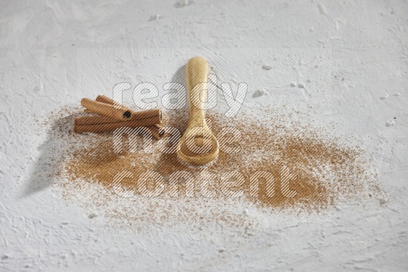 Cinnamon powder in a wooden spoon with cinnamon sticks and sprinkles powder on the flooring on white background