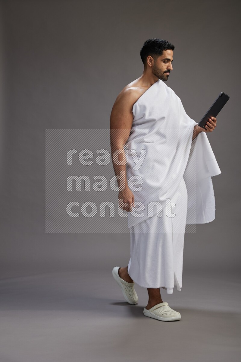 A man wearing Ehram and holding a tablet on gray background
