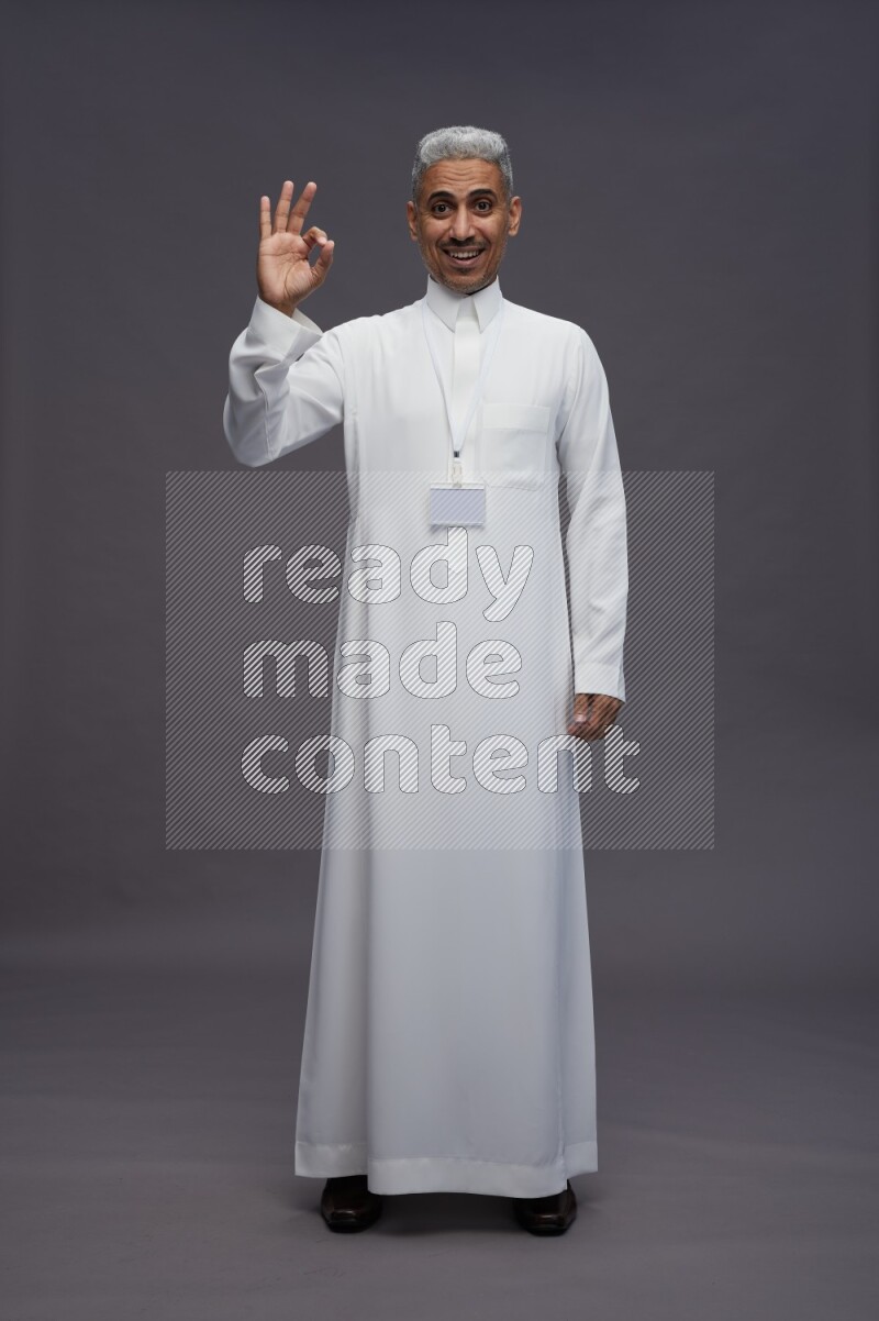 Saudi man wearing thob with neck strap employee badge standing interacting with the camera on gray background