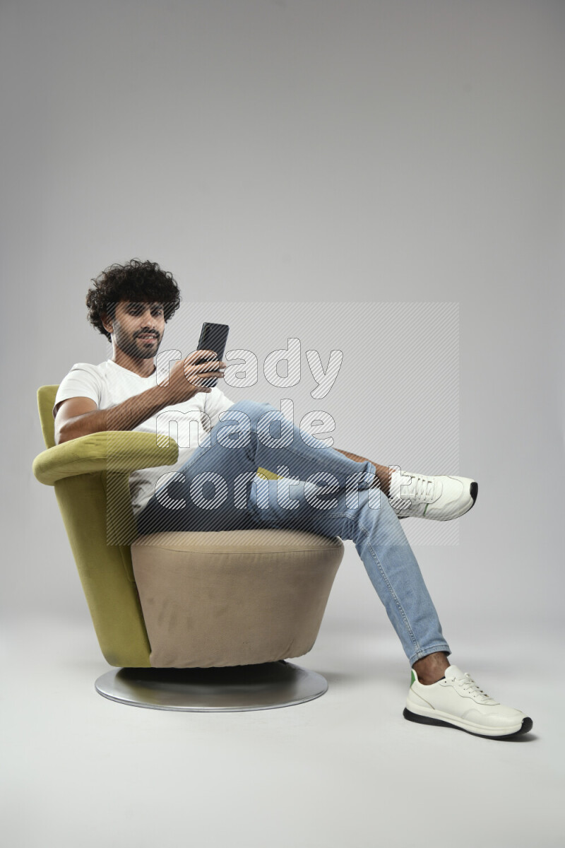 A man wearing casual sitting on a chair browsing on the phone on white background