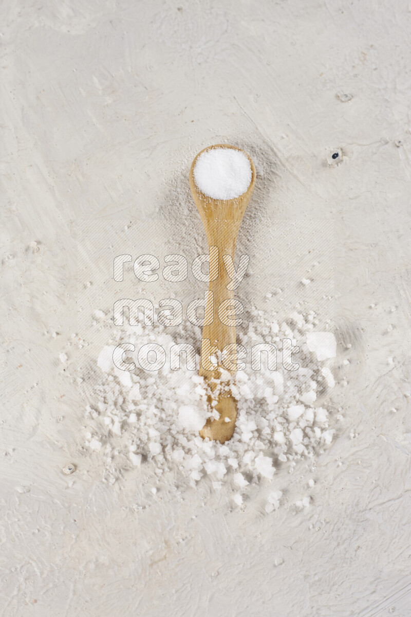 A wooden spoon full of white salt on white background