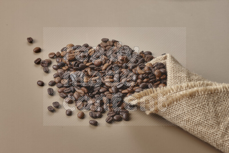 Spilled roasted coffee beans from its pack on beige background
