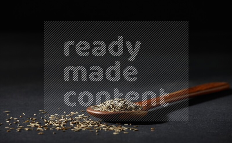 A wooden ladle full of cumin seeds on black flooring