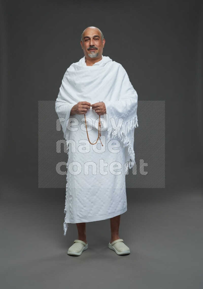 A man wearing Ehram Standing holding rosary on gray background