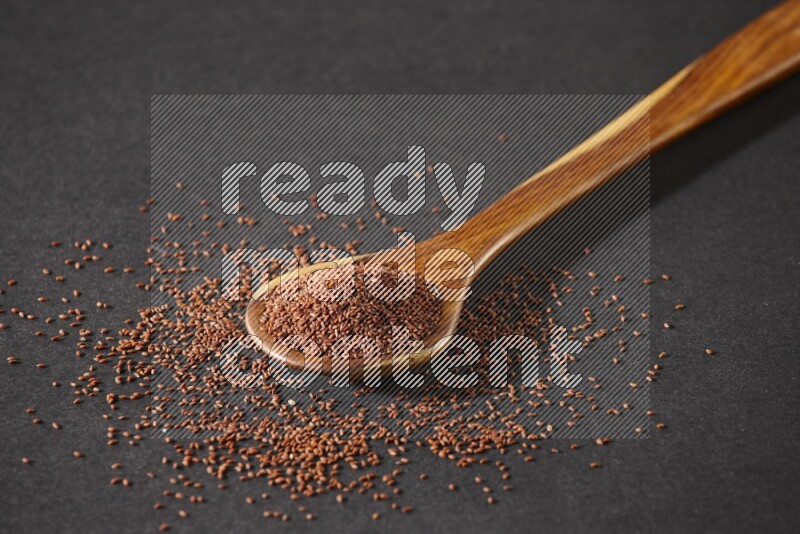 A wooden ladle full of garden cress seeds and seeds spread beside it on a black flooring