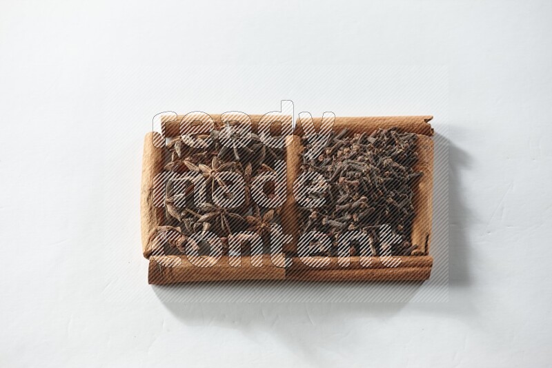 مربعان من أعواد القرفة ممتلئان بالقرنفل واليانسون النجمي علي خلفية بيضاء