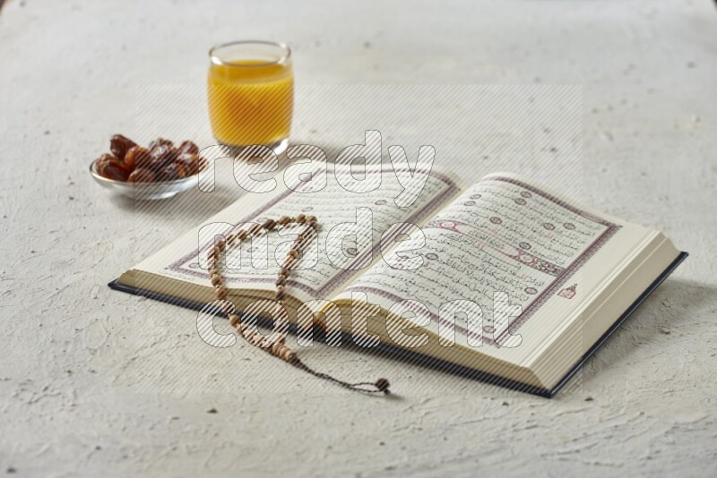 Quran with dates, prayer beads and different drinks all placed on textured white background