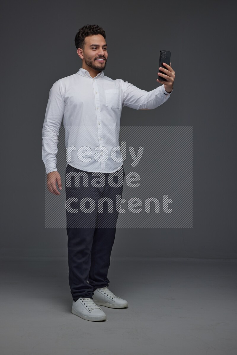 A man wearing smart casual and taking selfie with his phone eye level on a gray background