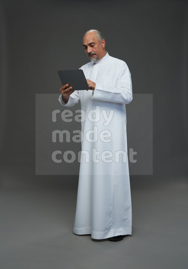 Saudi man without shomag Standing working on tablet on gray background