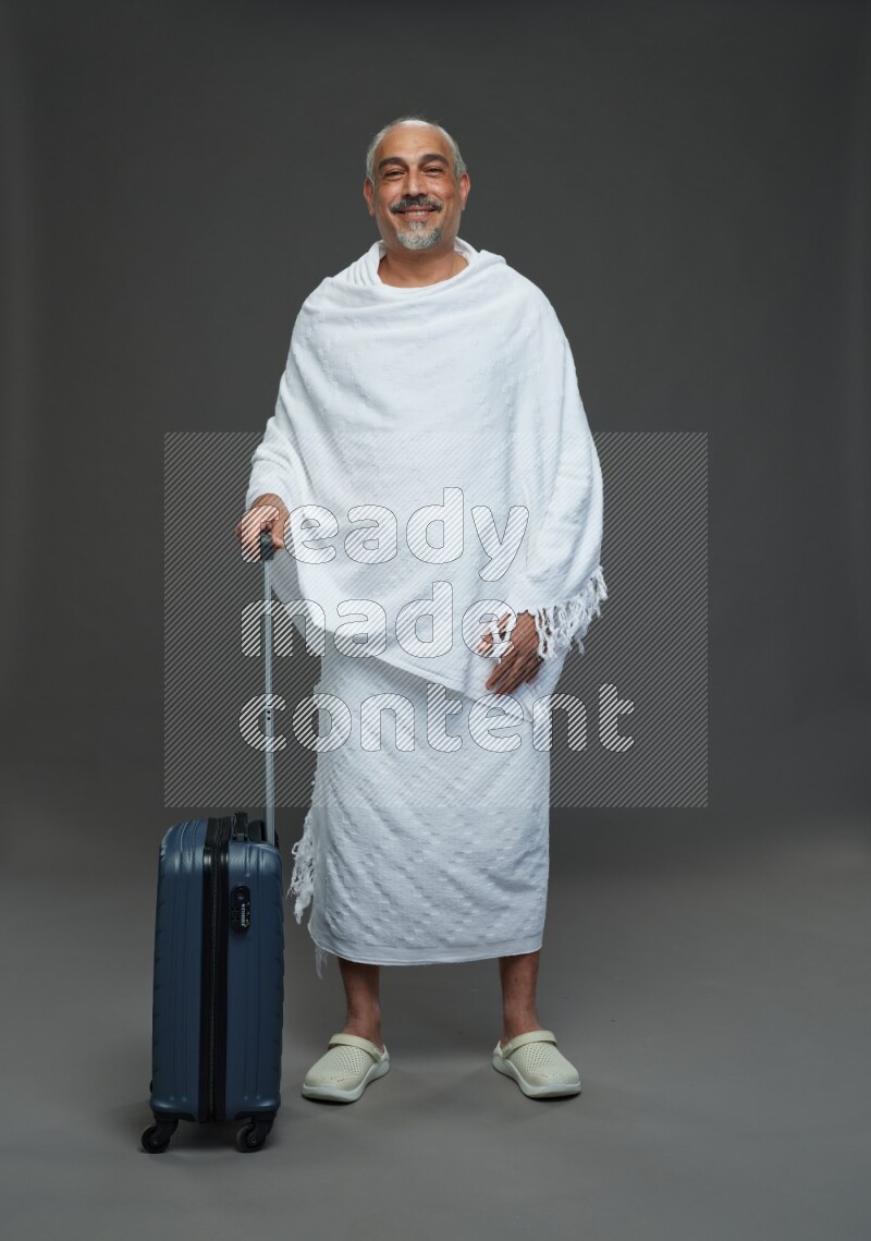 A man wearing Ehram Standing holding traveling bag on gray background