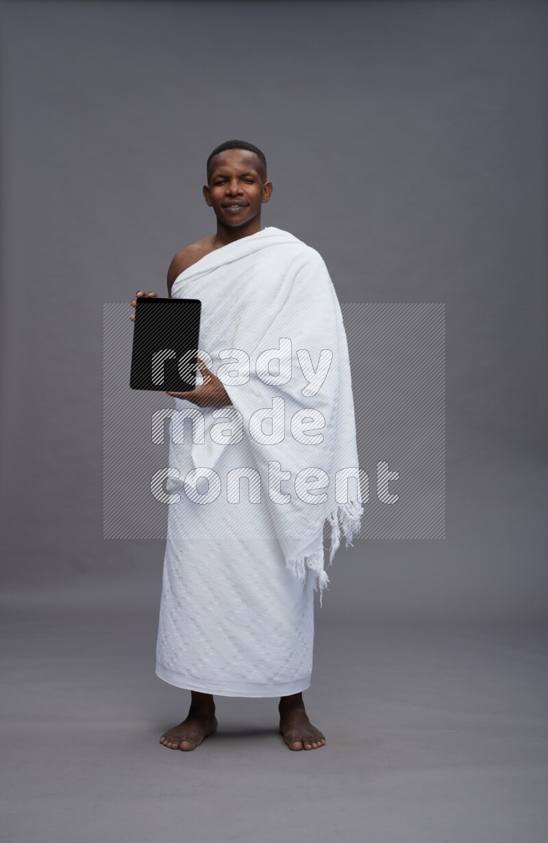 A man wearing Ehram Standing showing tablet to camera on gray background