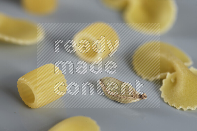 Raw pasta with different ingredients such as cherry tomatoes, garlic, onions, red chilis, black pepper, white pepper, bay laurel leaves, rosemary, cardamom and mushrooms on light blue background