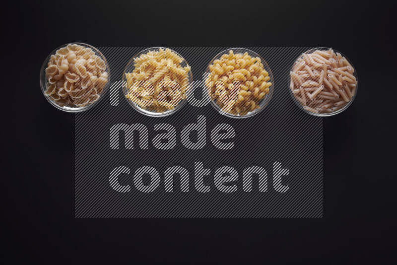 Different pasta types in glass bowls on black background