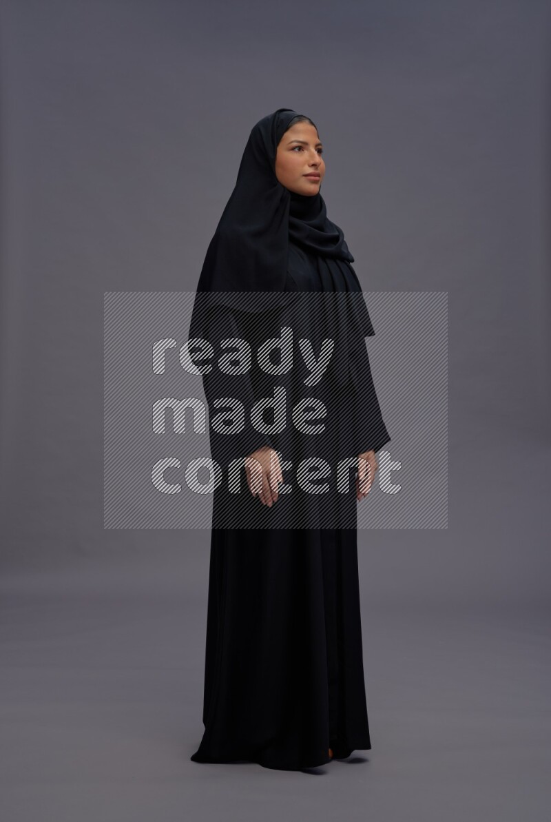 Saudi woman wearing Abaya standing interacting with the camera on gray background