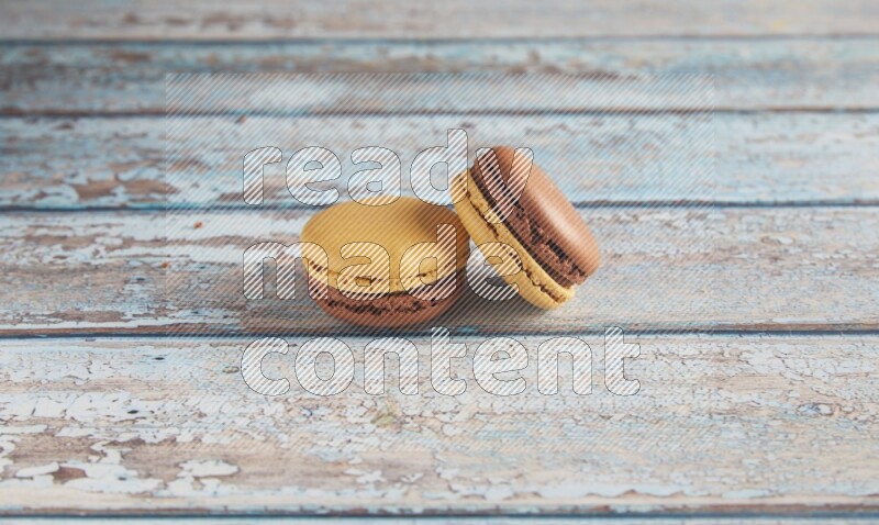 45º Shot of two Yellow and Brown Chai Latte macarons on light blue wooden background