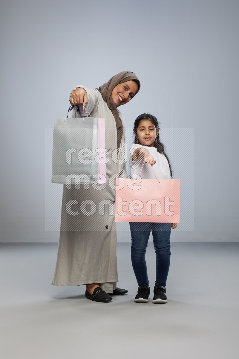 Mom and daughter holding shopping bags on gray background
