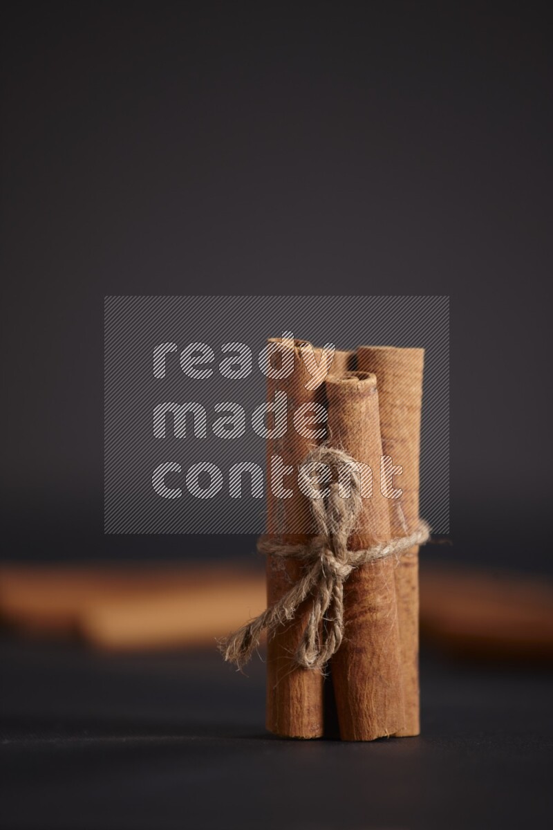 4 Cinnamon sticks stacked and bounded with more sticks in the background on black flooring