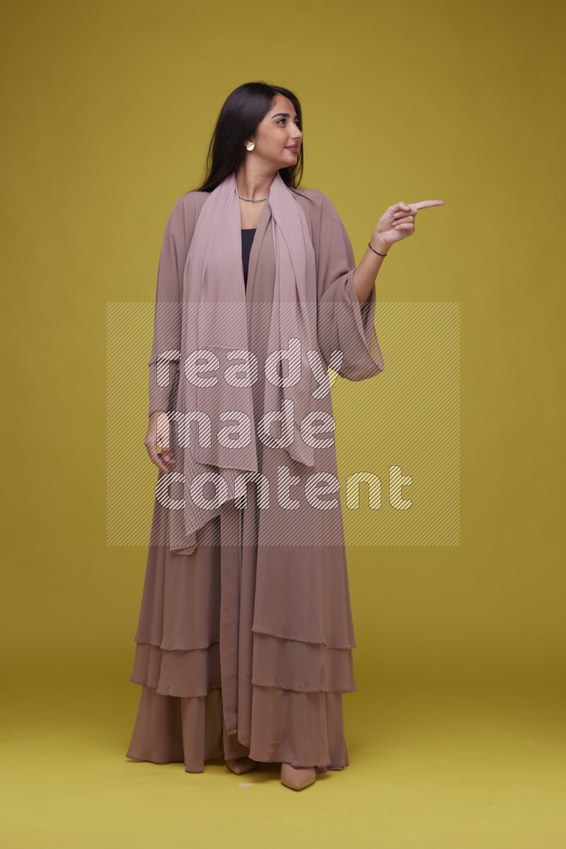 A woman Pointing on a Yellow Background wearing Brown Abaya